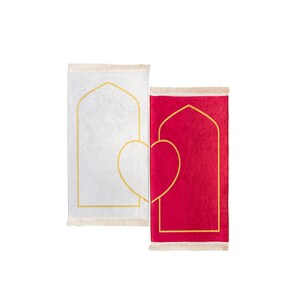 May include: Two prayer rugs, one white and one red, are displayed side by side. Each rug features a gold arched design and a gold heart shape. The rugs have a fringed edge.