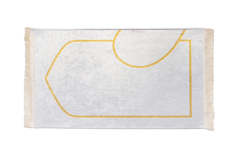 May include: A rectangular prayer rug with a white background and a gold geometric design. The rug has a textured surface and fringed edges. The gold design outlines a central rectangular shape and a curved top.
