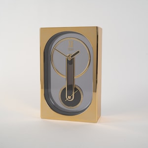May include: A gold-coloured clock with a unique design. The clock face is oval-shaped and has a black and silver design. The clock hands are black and the clock face is grey.
