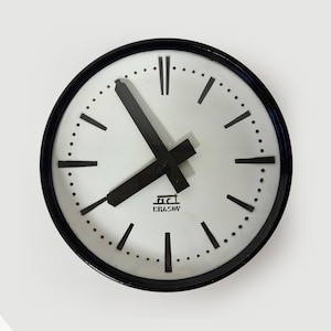 May include: A round wall clock with a white face and black hands and markers. The clock has a black bezel and the word "KRAKOV" is printed at the bottom of the clock face.