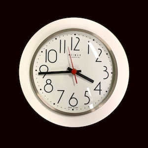 May include: A white round clock with black hands and black numbers on a white face. The clock face has the text "WEIMAR QUARTZ" and "MADE IN GDR".