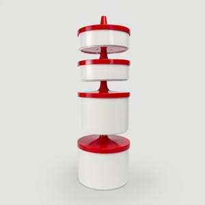 Op de afbeelding: Een verticale stapel van vier cilindervormige witte containers met glanzende rode deksels. Elke container wordt gescheiden door een rode centrale as, waardoor een gelaagde torenstructuur ontstaat. Het ontwerp heeft een wit en rood kleurenschema.