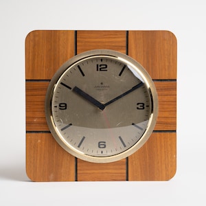 May include: A square wooden clock with a gold-toned face and black hands. The clock face has the text "JUNGHANS TIME" printed on it.