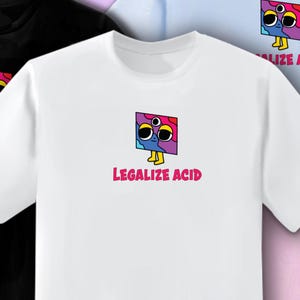 Può includere: T-shirt bianca con un personaggio dei cartoni animati colorato con tre occhi e la scritta "LEGALIZE ACID" in rosa. Il disegno è centrato sul davanti della maglietta. La maglietta è realizzata in un materiale morbido.