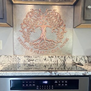 Puede incluir: Una placa de pared rectangular de metal con un diseño de árbol de la vida en relieve de color cobre con raíces y ramas intrincadas. El texto YESHUA'S HEART - OUR HOME está grabado en letras de color cobre sobre un fondo plateado texturizado.