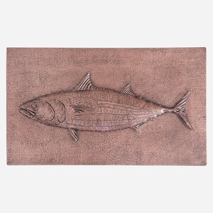 May include: A copper wall sculpture of a fish with a textured surface. The fish is in a raised relief style and has a detailed design.