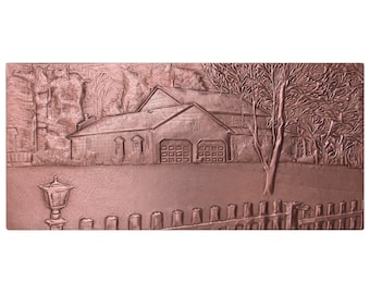 May include: A rectangular copper-toned metal wall plaque featuring a detailed embossed scene of a two-story house with a two-car garage, a front lawn, a picket fence, and a lamp post. The relief design captures the architectural details of the home.