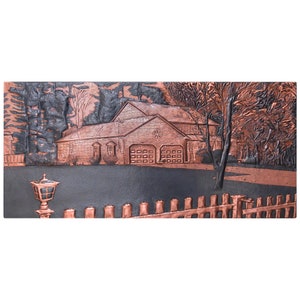 Puede incluir: Una escultura en relieve de cobre que representa una casa con un garaje doble, una valla y una farola en el jardín delantero. La casa está rodeada de árboles.