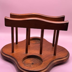 Puede incluir: Un portavasos y servilletero de madera vintage. El soporte es de madera marrón oscuro y presenta un diseño curvo único. Tiene dos piezas superiores curvas y varios soportes verticales, con dos recortes circulares.