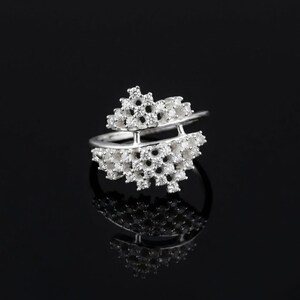 May include: A silver ring with a unique design, featuring two tiers of small, round settings, likely for gemstones. The ring has a modern, open design with a reflective surface, set against a black background.