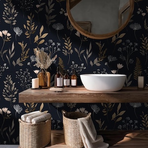 May include: A bathroom scene featuring a dark blue floral wallpaper with gold and white accents. A wooden shelf holds a white sink, brown bottles, and candles. Wicker baskets with towels sit below. A round wooden mirror hangs above.
