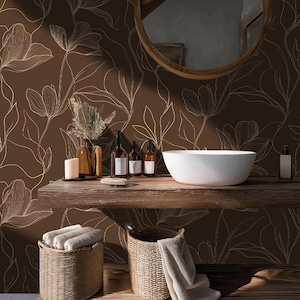 Peut inclure: Intérieur de salle de bain avec papier peint floral marron et dessin au trait blanc. Une étagère en bois supporte un lavabo blanc, des bouteilles, des bougies et un vase avec des fleurs séchées. Des paniers en osier avec des serviettes sont en dessous.