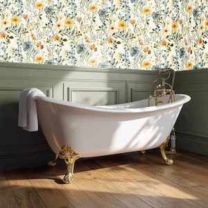 Könnte beinhalten: Eine weiße Badewanne mit Löwenfüßen und goldfarbenen Akzenten und Armaturen. Die Wanne steht vor einer Wand mit floraler Tapete in Gelb-, Blau- und Orangetönen. Ein weißes Handtuch hängt am Rand der Wanne.
