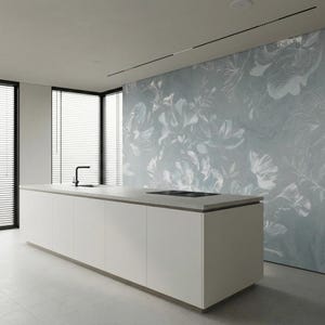 May include: Modern kitchen with a large white island and a light gray countertop. A black faucet and cooktop are visible. The wall features a floral mural in shades of blue and white. Large windows with black blinds provide natural light.