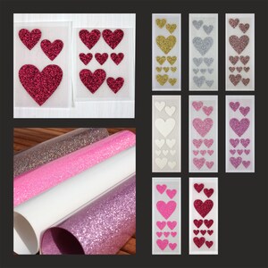 Könnte beinhalten: Eine Auswahl an herzförmigen Glitzeraufklebern in Gold, Silber, Rosa und Rot. Rollen aus Glitzerpapier in Silber, Rosa, Weiß und Lila sind ebenfalls zu sehen. Diese Bastelmaterialien eignen sich ideal für Scrapbooking-Projekte.