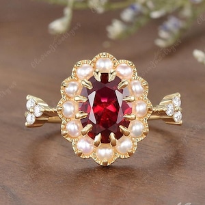 May include: A gold ring with a large oval ruby gemstone surrounded by a halo of small white pearls. The ring has a delicate band with small diamonds on each side.