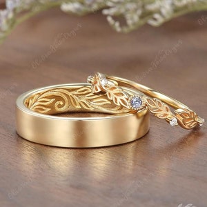 May include: A pair of gold wedding bands with a delicate leaf design. The band on the left has a smooth surface, while the band on the right has a row of small diamonds set in the leaves.