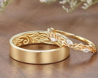 May include: A pair of gold wedding bands with a leaf design. The band on the left has a simple leaf design, while the band on the right has a more intricate design with small diamonds.