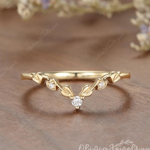 May include: A gold V-shaped ring featuring a delicate leaf-inspired band design. The ring is accented with three small, clear round-cut stones set within the metal leaves, with one stone at the center point and two stones on the sides.
