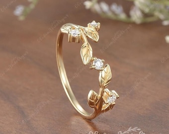 May include: A delicate gold ring with a vine design featuring small clear stones. The ring is made of gold and has a leaf pattern.
