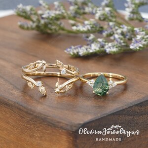 May include: Two gold rings with a delicate leaf design and small clear stones. The ring on the left is a split ring with two bands. The ring on the right has a pear-shaped green stone with clear stones on either side.