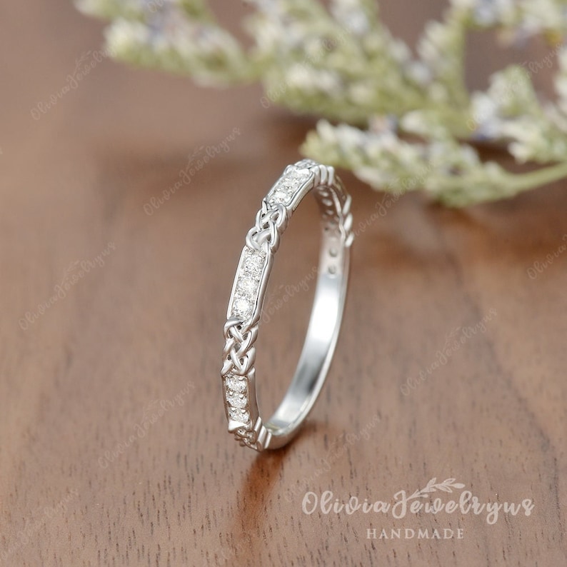 May include: A delicate silver wedding band with a Celtic knot design and a row of small sparkling diamonds.