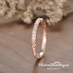 May include: A delicate rose gold wedding band with a braided design and a row of small diamonds.
