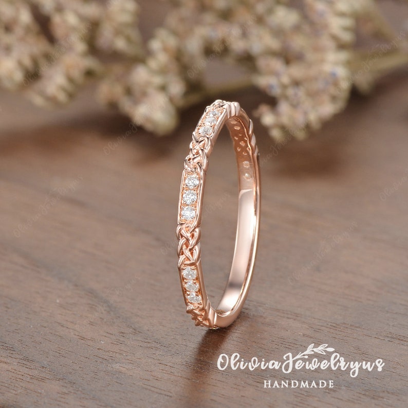 May include: A delicate rose gold wedding band with a braided design and a row of small diamonds.