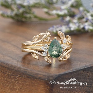 May include: Gold ring set with a pear-shaped green moss agate gemstone surrounded by small diamonds. The ring features a delicate design of leaves and bees.