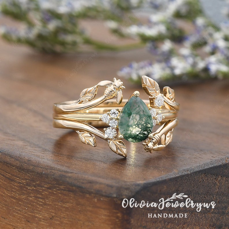 May include: Gold ring set with a pear-shaped green moss agate gemstone surrounded by small diamonds. The ring features a delicate design of leaves and bees.