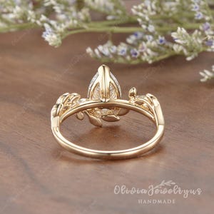 May include: A gold ring with a pear-shaped diamond set in a delicate floral design. The ring is handmade and features intricate details.