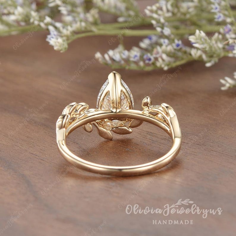 May include: A gold ring with a pear-shaped diamond set in a delicate floral design. The ring is handmade and features intricate details.