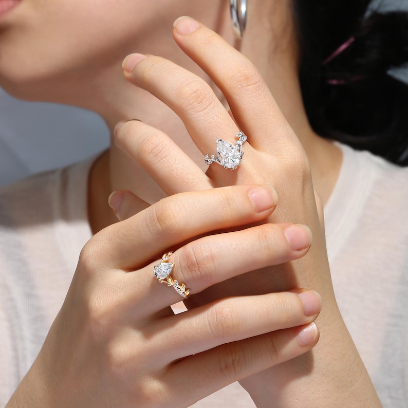 May include: Two pear-shaped diamond rings with intricate floral designs. The ring on the left has a gold band and the ring on the right has a silver band.