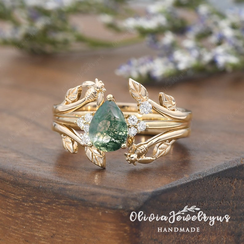 May include: A gold ring with a pear-shaped green moss agate gemstone surrounded by small diamonds. The ring features a delicate design of leaves and vines.