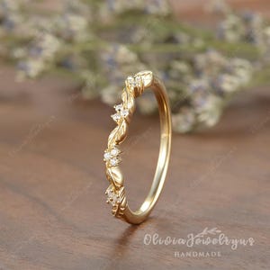 May include: A delicate gold wedding band with a twisted design and small diamonds set in the band. The band is handcrafted and has a subtle floral pattern.