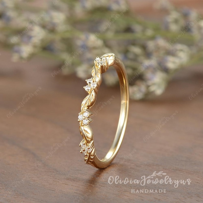 May include: A delicate gold wedding band with a twisted design and small diamonds set in the band. The band is handcrafted and has a subtle floral pattern.