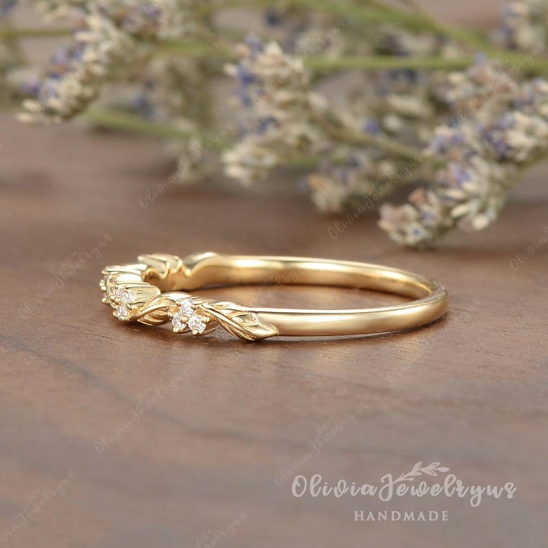 May include: A delicate gold band with a floral design and small diamonds. The band is on a wooden surface. Olivia Jewelryrus HANDMADE.