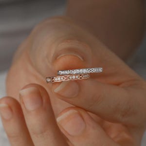 May include: Two delicate diamond wedding bands, one in rose gold and one in white gold, with intricate designs. The bands are stacked on top of each other.