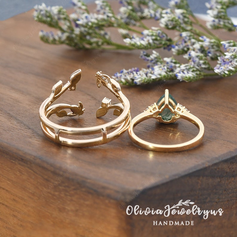 May include: Two gold rings with a green gemstone and a delicate leaf design. The rings are on a wooden surface. Olivia Jewelryrus HANDMADE.