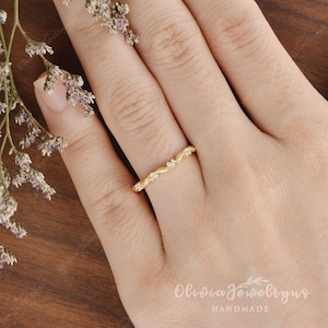 May include: A delicate gold band ring with a vine design and small clear stones. The ring is on a model's finger.