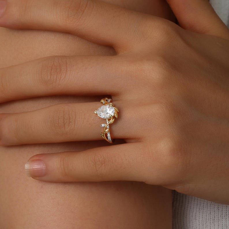 May include: A gold ring with a pear-shaped clear stone set in a delicate vine design.