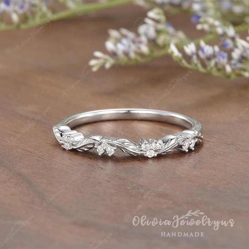 May include: A delicate silver band with a twisting vine design and small diamonds. The band is handmade and features a floral motif.