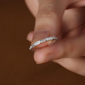 May include: A silver band ring with a Celtic knot design and small clear stones set in the band.