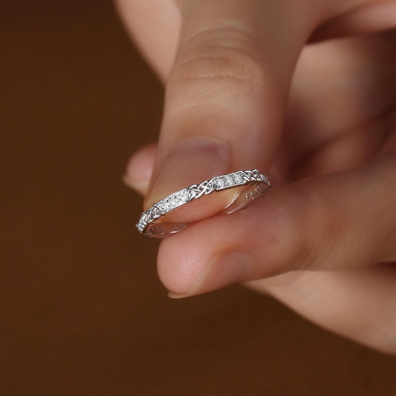 May include: A silver band ring with a Celtic knot design and small clear stones set in the band.