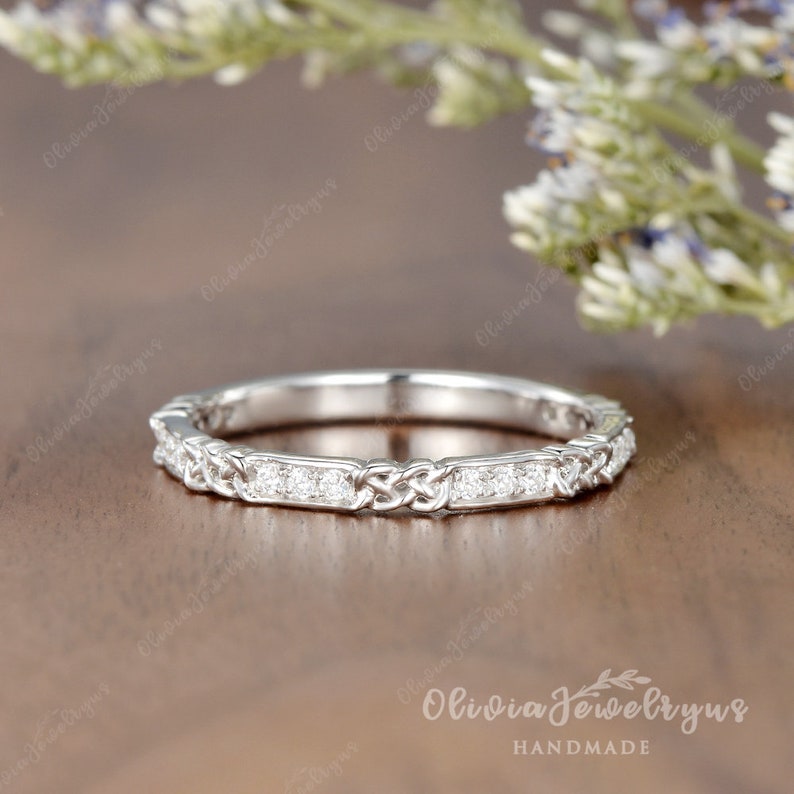 May include: A delicate silver wedding band with a Celtic knot design and a row of small diamonds.