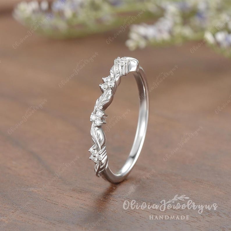 May include: A delicate silver band with a floral design and small clear stones. The band is curved and has a subtle twist.