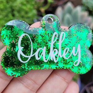 May include: Green glitter dog tag with a bone shape and the name "Oakley" written in white.