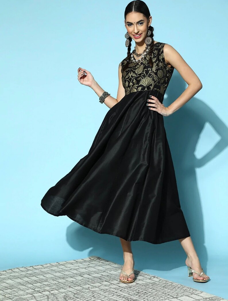 May include: A black sleeveless dress with a gold floral print bodice and a flowing skirt. The dress is worn by a model with long dark hair and gold earrings.
