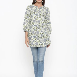 May include: A white cotton tunic top with a blue and green floral print. The top has a round neckline and three-quarter sleeves. The model is wearing the top with blue jeans.