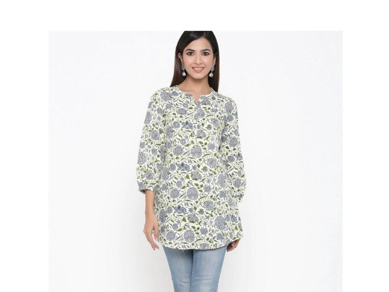 May include: A white tunic top with a blue and green floral print. The top has a round neckline and three-quarter sleeves.